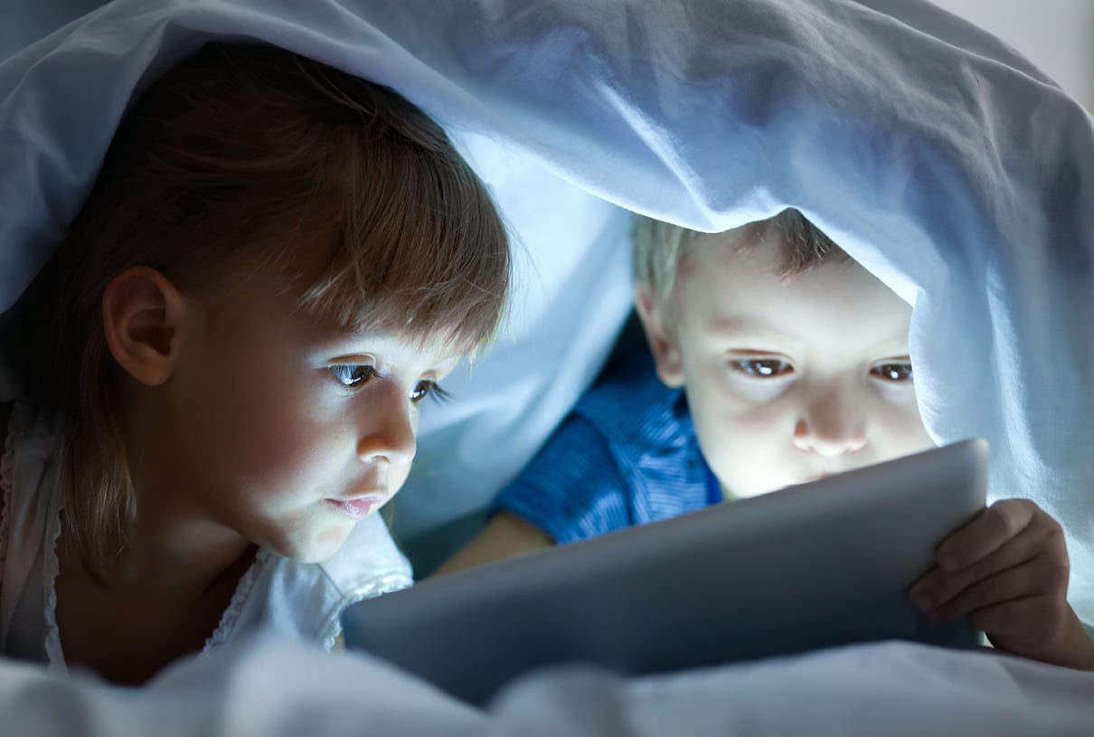 Niños escondidos en la cama mirando pantallas